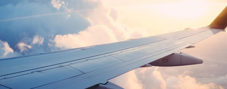 Wing of an airplane in the air with clouds and the sun in the background. 