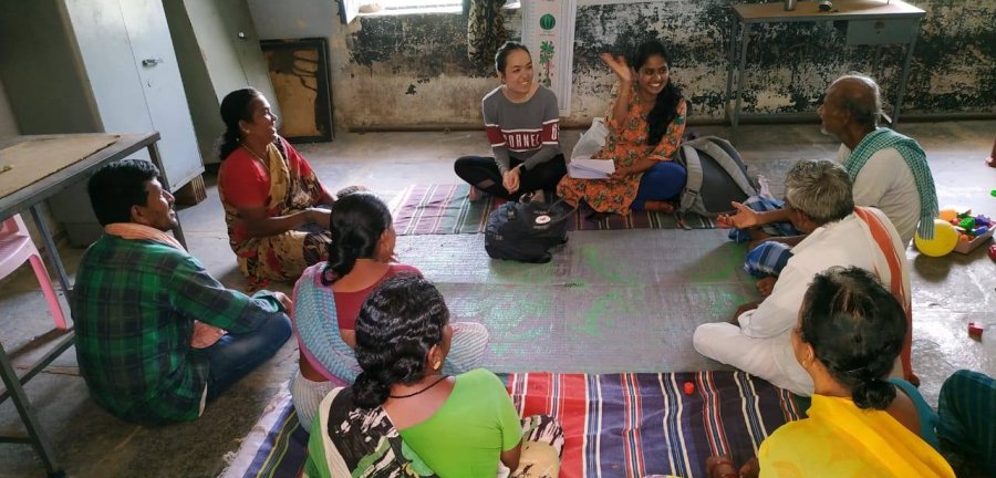 A Cornell student sitting on the floor with a circle of people in traditional Indian attire.
