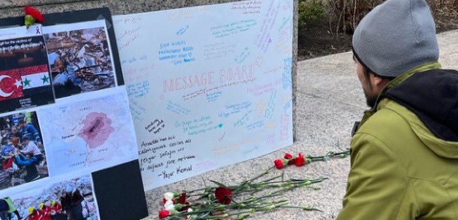 Man sitting at base of statue looking a poster and flowers.