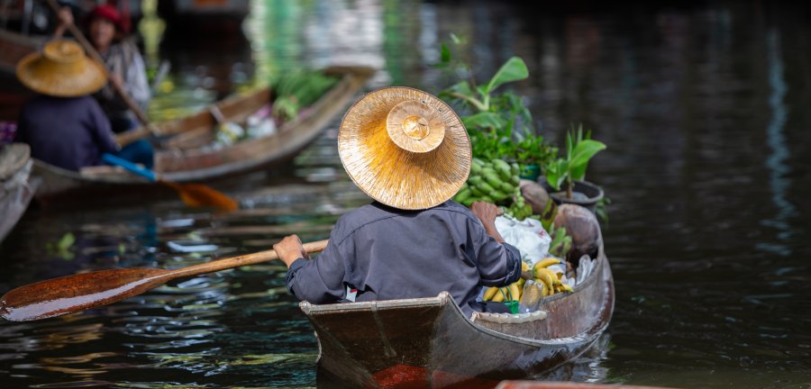 Person wearing a straw hat, paddling in the Damnoen Saduak floating market, Thailand
