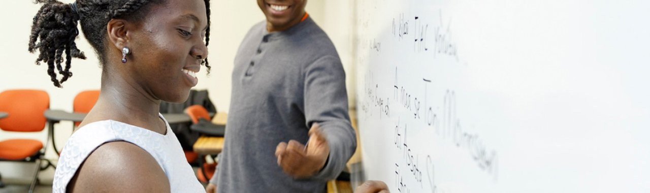 Student writing on whiteboard, instructor in background