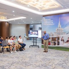 Students seated on the left and a speaker on the right with a portable monitor and a large banner welcoming the students.