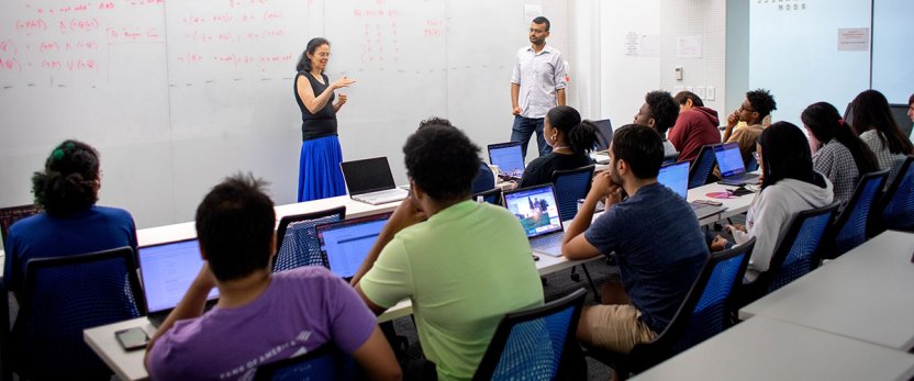 Faculty member in front of a white board teaching a class. 