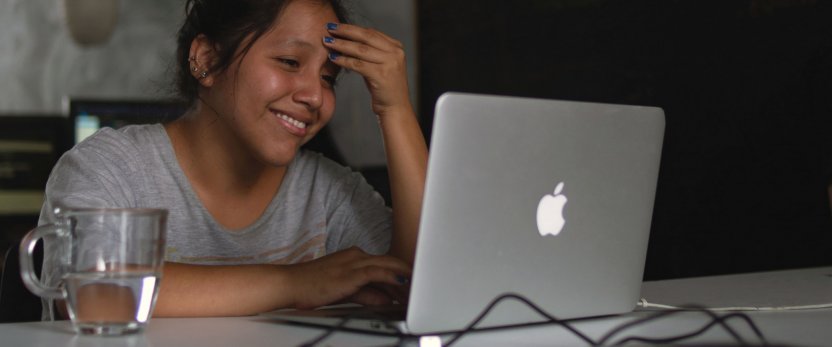 Seated student looking at a laptop with a cup of water on the table.