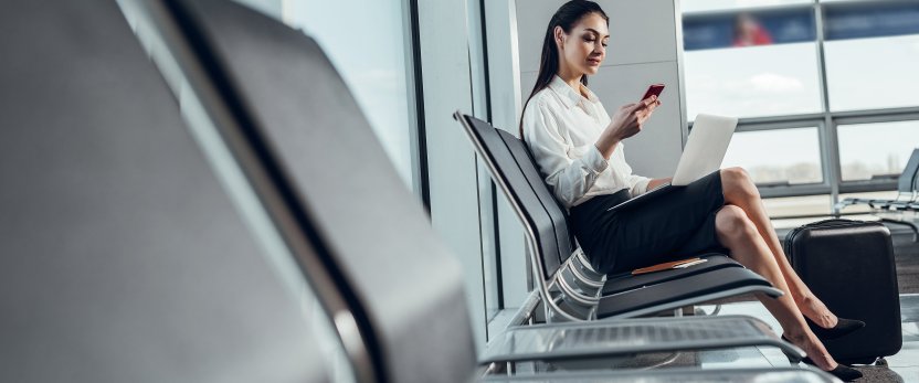 Woman sitting in an airport using her phone and laptop.