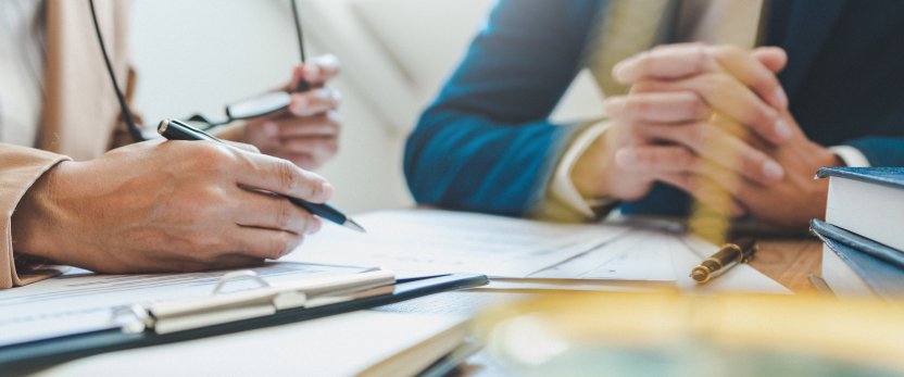View of two people's hands resting on a desk with paperwork.