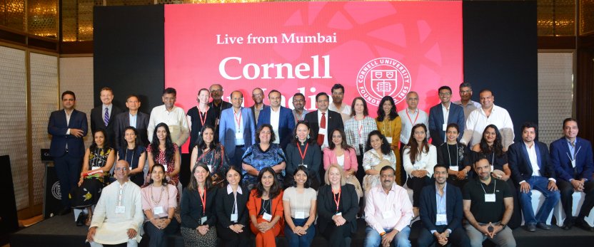 A crowd posing in front of of a banner that reads, Live from Mumbai, Cornell."