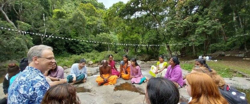Andrew Willford sitting with Cornell studens and Indian locals in a wooded setting.