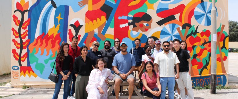 Group of people standing in front of a colorfully painted wall. 