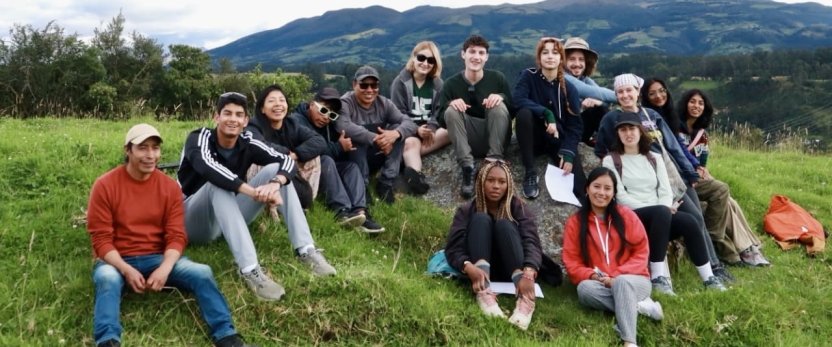 Students and a local guide sitting outside with mountains in the background.