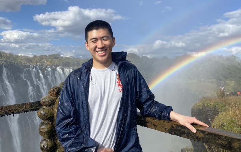 Charles standing at a lookout point with a waterfall and rainbow in the background.