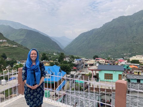 Phoebe standing on a balcony overlooking a town with green mountains in the background.