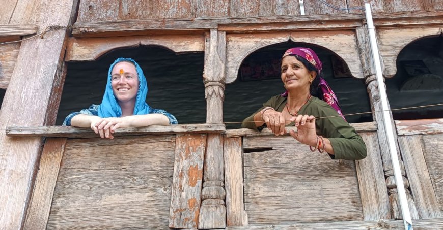 Phoebe and another women leaning out of an open wooden balcony. 