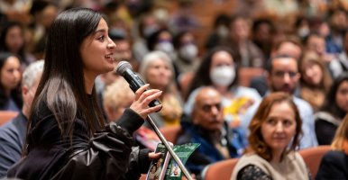 A student is holding a microphone at a lecture and asking a question in front of a full house.