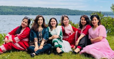 Six students sitting on the grass in front of Cayuga Lake. 