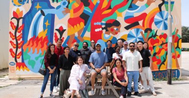 Group of people standing in front of a colorfully painted wall. 