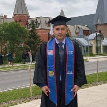 Farid in graduation garb standing in front of Sage Hall.