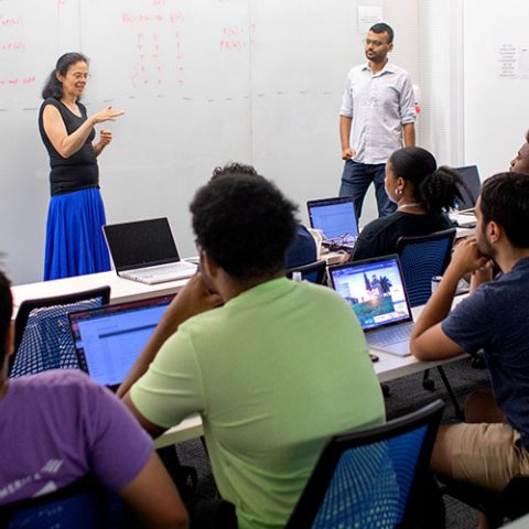 Faculty member in front of a white board teaching a class. 
