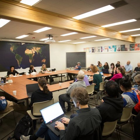 Faculty and students sitting around a square table with additional rows of seats on two sides.