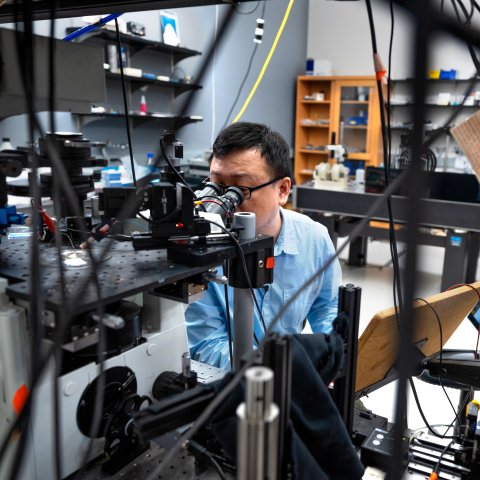 Man looking through a microscope in a lab setting.